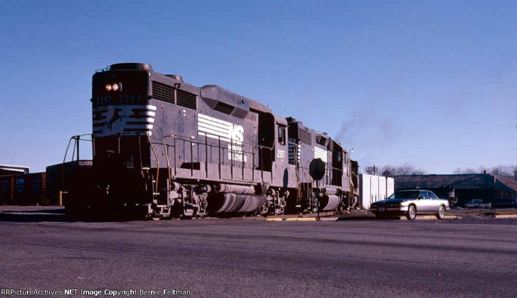 Norfolk Southern GP30 #2557, GP38 #2818 and a U23B lead a Dothan, AL bound train out of the yard, past the old passenger station in the background, and around the 90 degree curve to street running on Roosevelt Avenue 